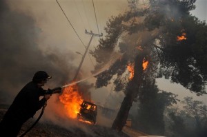 A firefighter sprays water on a burning tree as a car burns near Agios Stephanos, a suburb north of Athens, on Sunday, Aug. 23, 2009. Thousands of local residents were involved in evacuations as the wind-driven fires destroyed homes and threatened several residential areas. (AP Photos/Nikolas Giakoumidis)